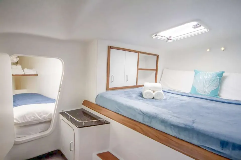 King cabin with a blue coverlet, rolled towels, and an overhead hatch