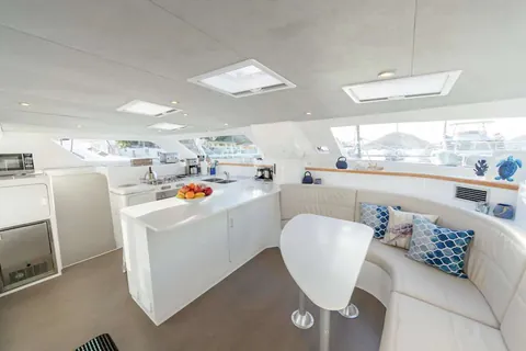 Salon with a curved white settee, a bar-height table, and the galley beyond